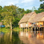 Late afternoon view of a shack on stilts in the Amazon rain forest with a beautiful reflection in the river